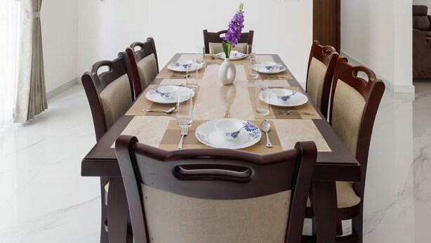 A dining room with a long table set for six, surrounded by chairs, a ceiling fan, and an air conditioning unit. - Casa Miro by Red Olive 4bhk Hebbal Bangalore (Bengaluru)