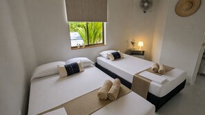 A hotel room with three beds, each with white linens and a single pillow. There is a window with a view of greenery outside, a bedside table with a lamp, and a fan on the wall. - Casa Encanto in Río Bonito | Nature, the river, and a relaxing family getaway in Melgar (Melgar)