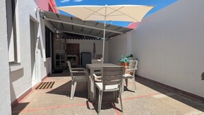 Eine Terrasse im Freien mit Tisch und Stühlen, einem überdachten Bereich und einem Blumentopf.