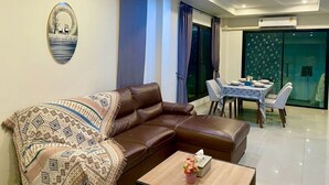 A modern living room with a brown leather sofa, a coffee table, and a dining area with a table set for two. - Best area near by shopping mall (Chiang Mai)