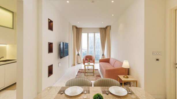A modern living room with a sofa, a TV, and a dining area with a table set for two. - Casa Opal by Red Olive1bhkleela Residency (Bengaluru)