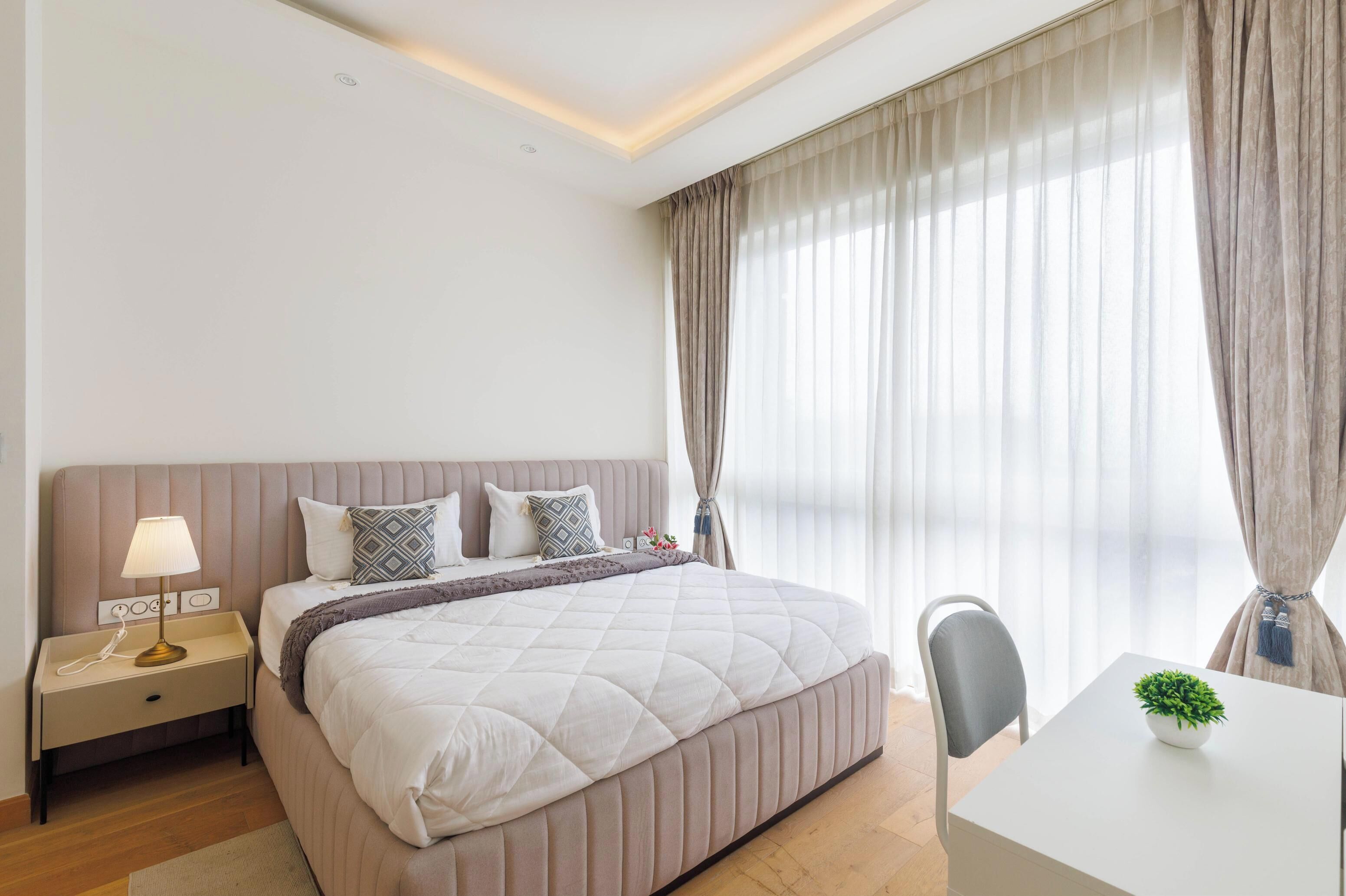Un dormitorio moderno con una cama grande, mesita de noche, lámpara y una pequeña mesa con una planta.