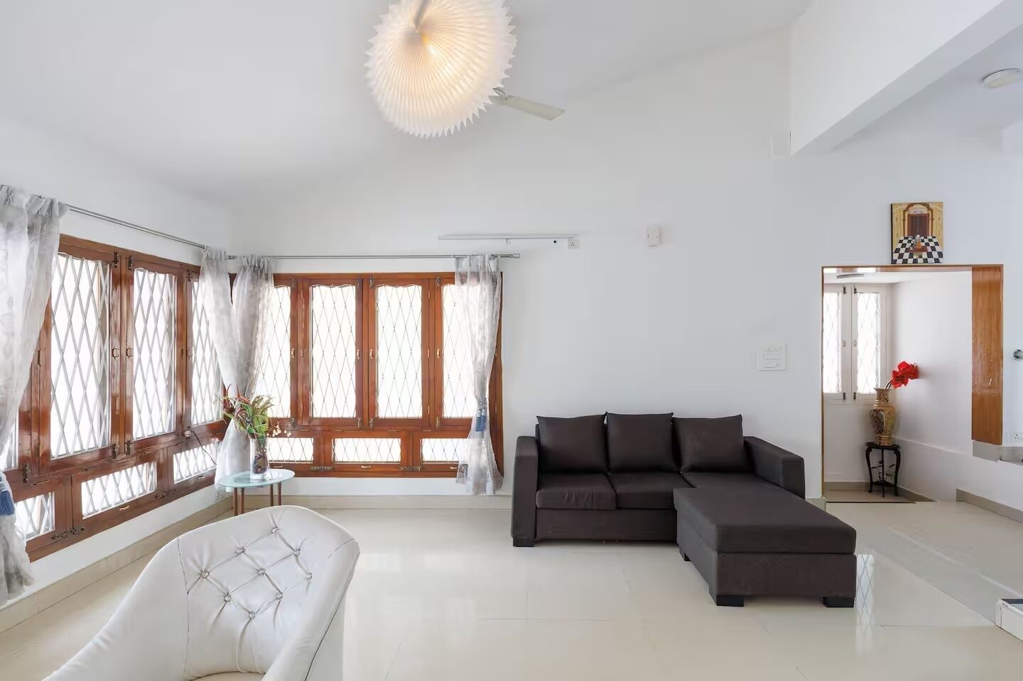 A modern living room with a sectional sofa, a white armchair, and a large window with curtains.