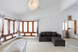 Un salon moderne avec un canapé d’angle, un fauteuil blanc et une grande fenêtre agrémentée de rideaux.