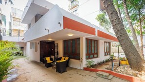 A modern two-story building with a flat roof, a balcony, and a patio area with outdoor furniture. - Casa Promenade by Red Olive 3bhk Frazer Town (Bengaluru)