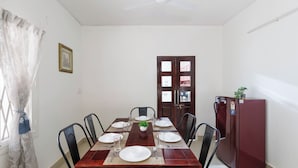 A dining area with a wooden table set for four, surrounded by chairs, a ceiling fan, and a refrigerator. - Casa Promenade by Red Olive 3bhk Frazer Town (Bengaluru)