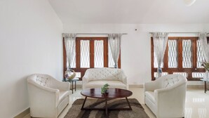 A living room with two white sofas, a round coffee table, and a large window with curtains. - Casa Promenade by Red Olive 3bhk Frazer Town (Bengaluru)