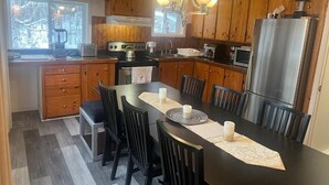 Une cuisine avec des meubles en bois, un réfrigérateur en acier inoxydable, une table à manger avec des chaises et un lustre.