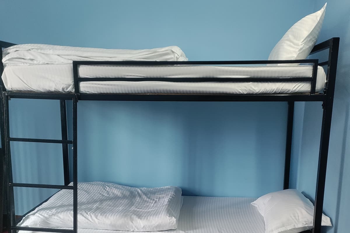 A bunk bed with white bedding, a wooden bench, and a red carpet.