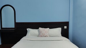 Una cama bien tendida con ropa blanca y dos almohadas, un cabecero oscuro y un espejo fijado a la pared.