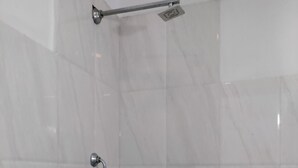 Un baño con azulejos de mármol blanco, cabezal de ducha y grifo.