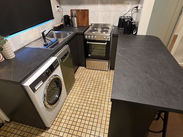 A compact kitchen with a washing machine, a stove, and a sink.