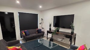 A modern living room with a glass coffee table, two sofas, a TV, and a small side table with a plant. - A Sporting Spot in Warm Sunshine (Sunshine North)