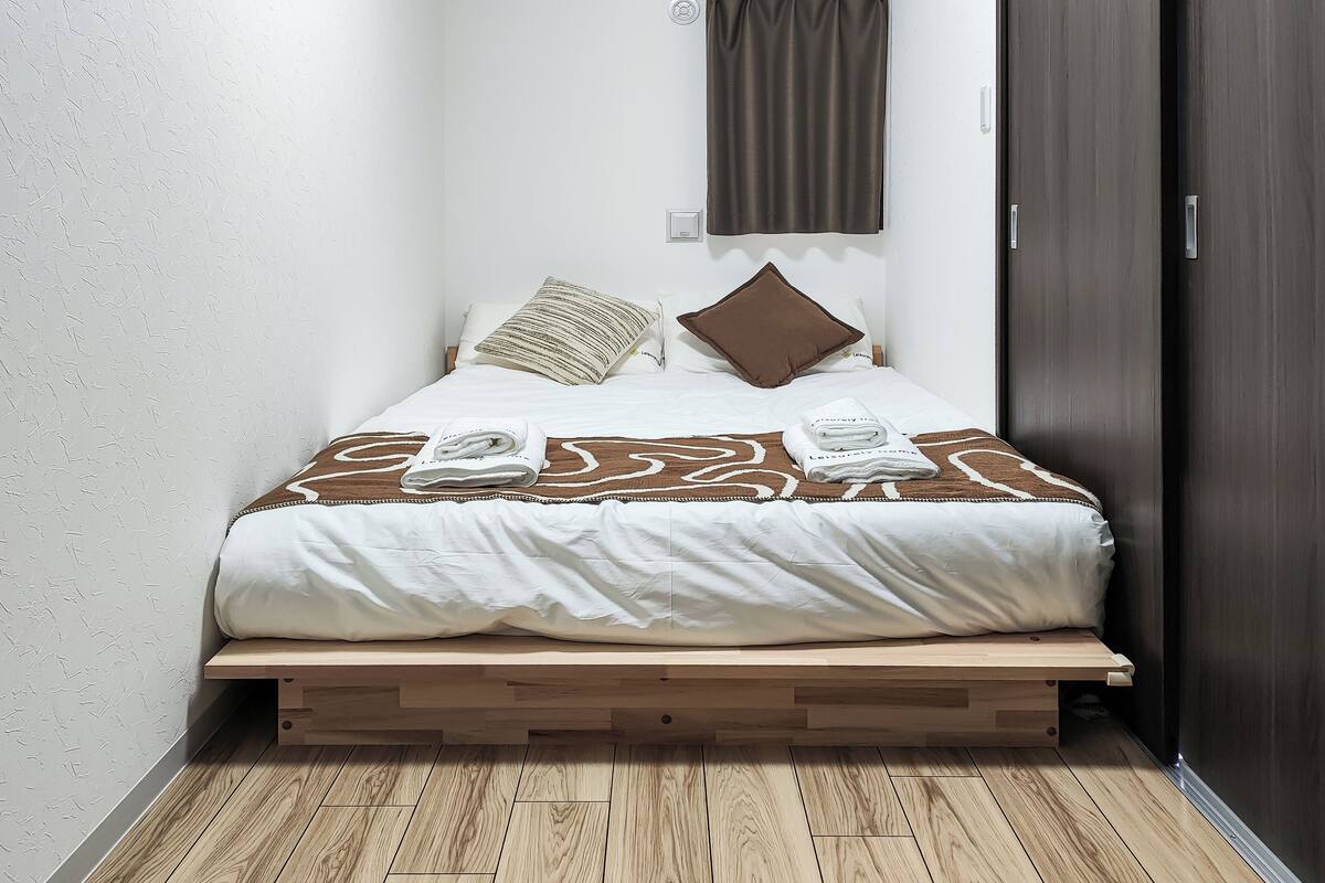 Ein kleines, ordentlich gemachtes Bett mit einer braun-weißen Bettdecke, einem hölzernen Plattformbett und einem dunkelbraunen Kleiderschrank.