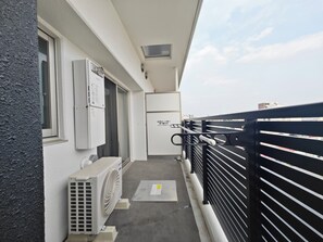 Un balcón con barandilla negra, unidad de aire acondicionado blanca, una ventana y una puerta.