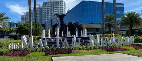 Et skilt med "The Magellan Newtown" i store bogstaver, omgivet af en anlagt område med palmer og en fontæne.