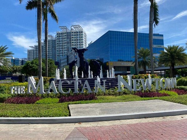 A sign with "The Magellan Newtown" in large letters, surrounded by a landscaped area with palm trees and a fountain. - OYO 1192 Rk Property Rentals (Lapu-Lapu)