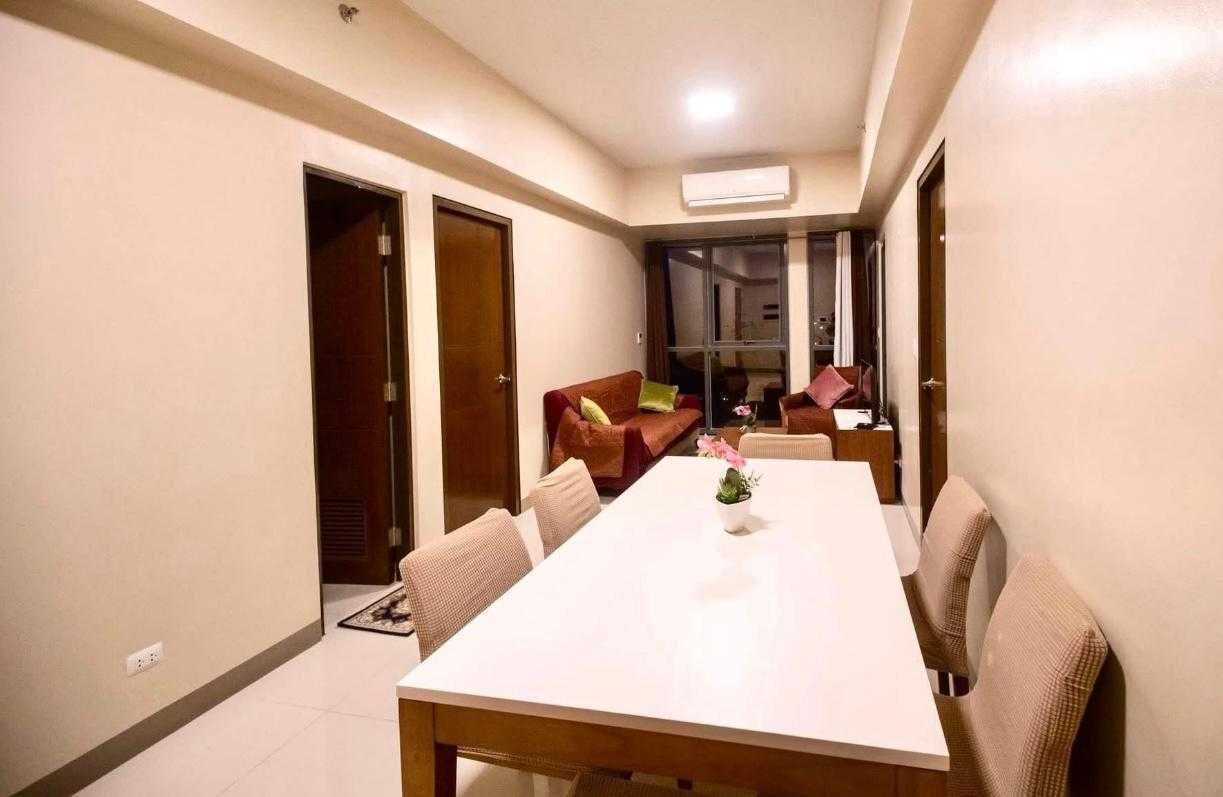 A modern living room with a large white dining table, comfortable seating, and a sliding glass door leading to a balcony.
