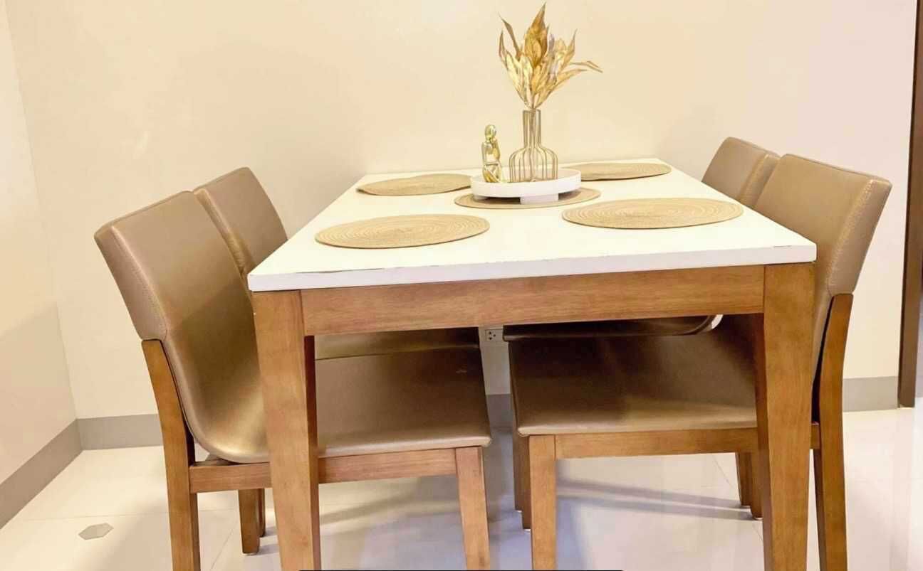 Una mesa de comedor con cuatro sillas, un florero con plantas secas y una pequeña estatua.