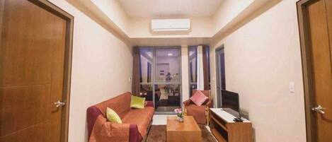 A compact living room with a sofa, coffee table, and TV, featuring a sliding glass door leading to another room.