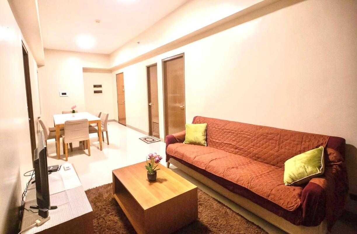 A living room with a red sofa, a wooden coffee table, a TV, and a dining area in the background.