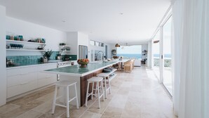 Una cocina moderna con una isla grande, taburetes blancos y vista al mar.