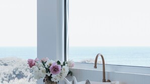 Un baño con un lavabo blanco, un florero con flores y vistas al océano.