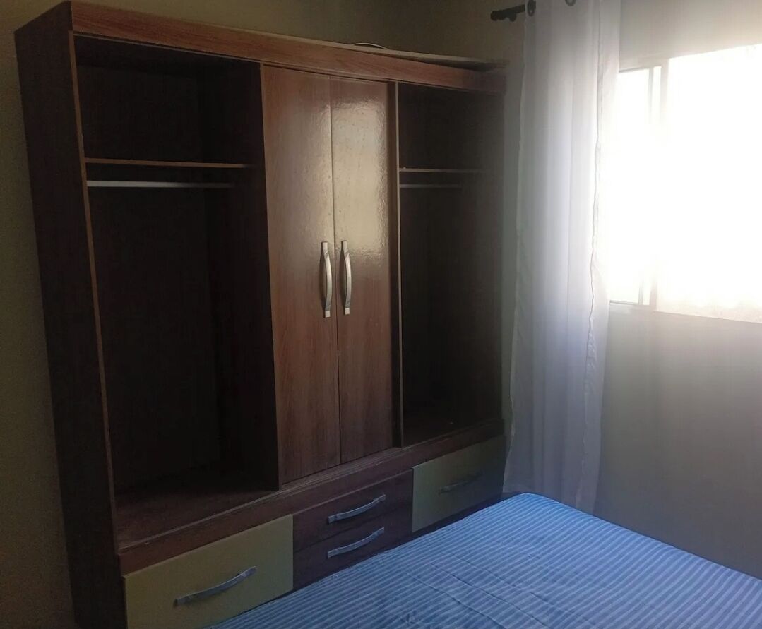 Ein Schlafzimmer mit großem Holzschrank, einem Bett mit gestreifter Bettdecke und einem Fenster mit durchsichtigen Vorhängen.