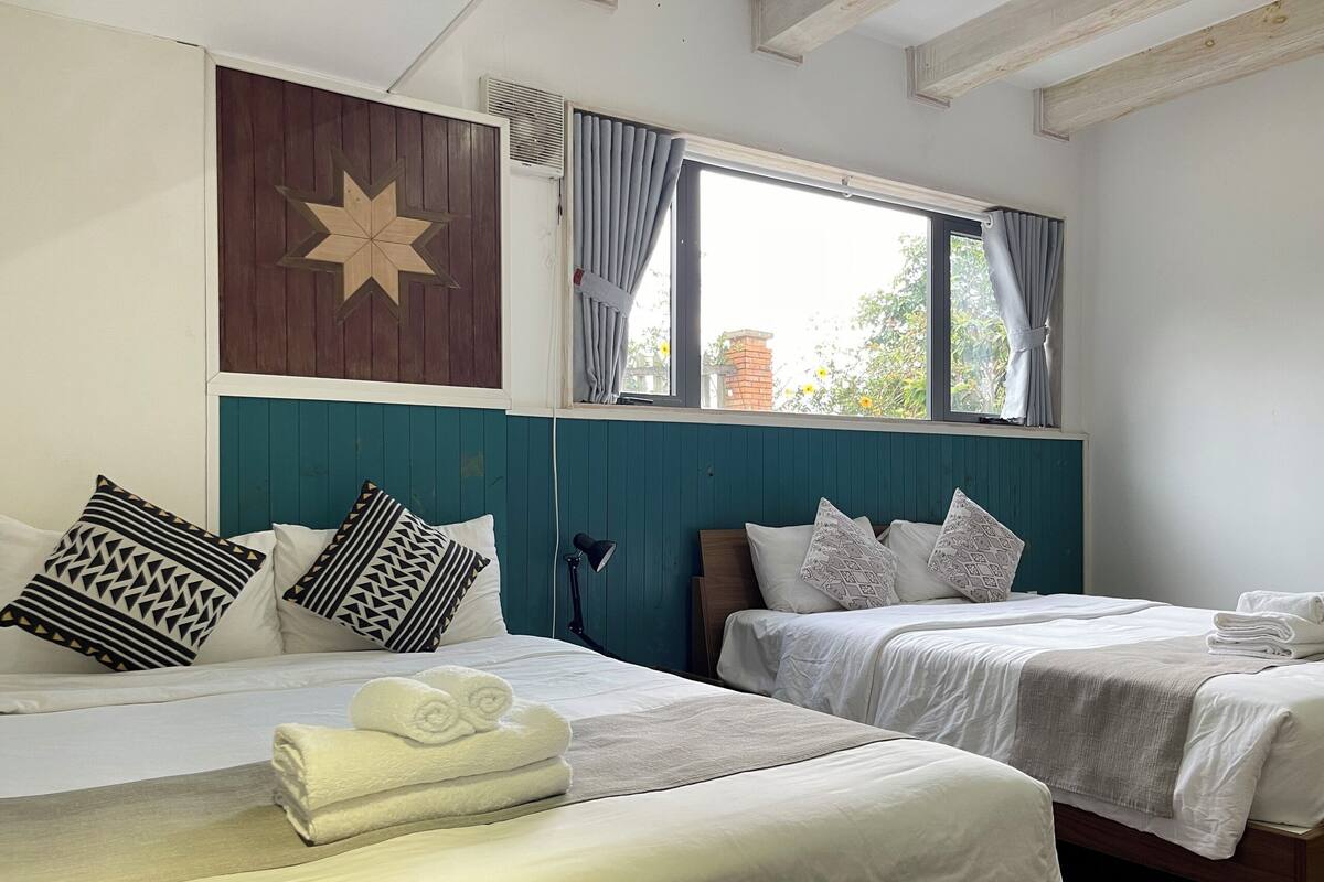 Habitación de hotel con dos camas, un adorno con forma de estrella en la pared, una ventana con cortinas y una lámpara.