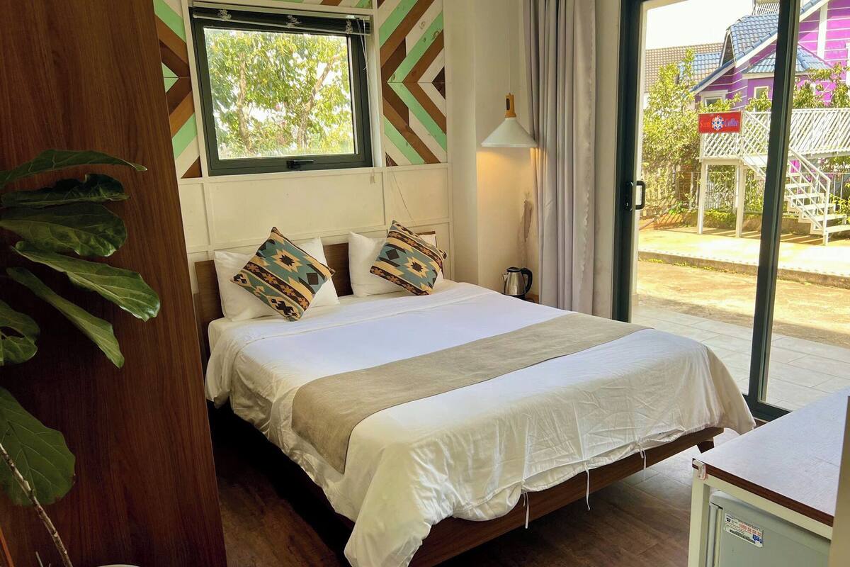 Habitación de hotel con cama, ventana, lámpara y vistas al exterior.