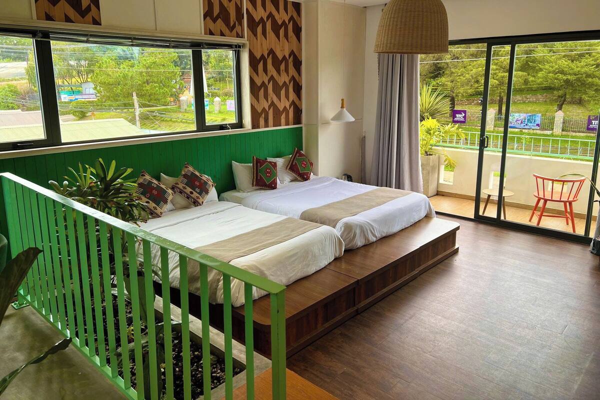 Habitación de hotel moderna con dos camas, una barandilla verde y vistas al exterior.