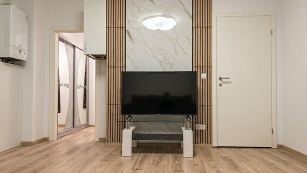 Una sala de estar moderna con un televisor de pantalla plana sobre un pedestal de vidrio, paneles de madera y una pared de mármol.