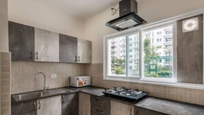 A kitchen with a gas stove, a sink, and cabinets. There is a window with a view of buildings outside. - The Urbanite Twins by Stayjadecminr Aster (Bengaluru)