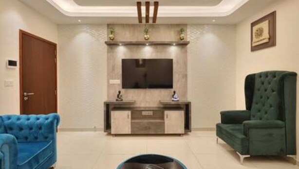 A living room with a flat-screen TV, a wooden entertainment unit, a blue sofa, a green armchair, and a round coffee table. - The Urbanite Twins by Stayjadecminr Aster (Bengaluru)