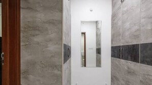 A narrow hallway with a wooden door frame on the left, a mirror on the right, and a tiled floor. - The Urbanite Twins by Stayjadecminr Aster (Bengaluru)