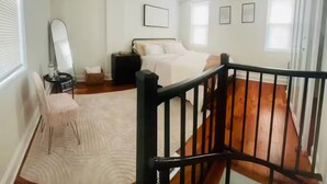 Een slaapkamer met een bed, een stoel, een bureau, een spiegel en een raam.