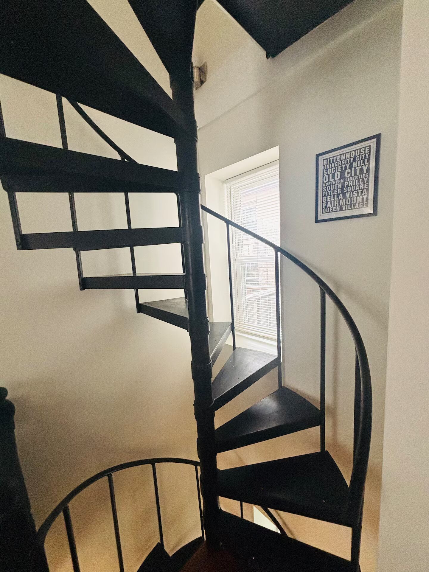 A spiral staircase with black railings and a window with blinds.