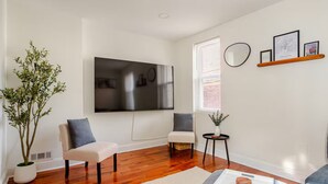 Een moderne woonkamer met een flatscreen televisie, twee fauteuils, een bijzettafeltje en een potplant.