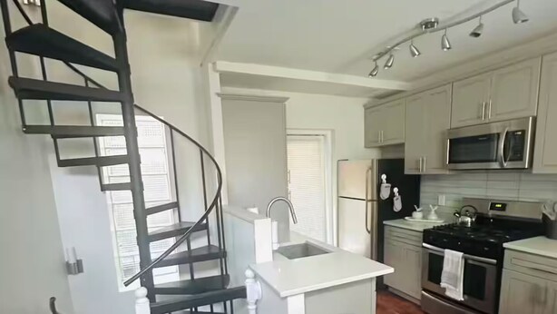 Een moderne keuken met een centraal eiland, roestvrijstalen apparatuur en een wenteltrap.