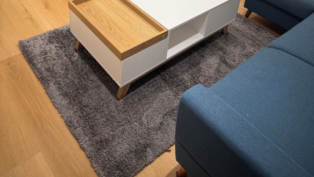 Ein modernes Wohnzimmer mit einem Flachbildfernseher auf einem Holz-TV-Schrank, einem weißen Couchtisch und einem blauen Sofa.