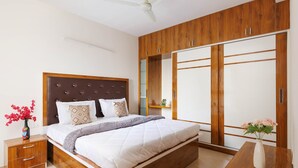 A bedroom with a bed, wooden wardrobe, bedside table, and a nightstand with a vase. - Willow Height by Red Olive30min to Airport Veg (Bengaluru)