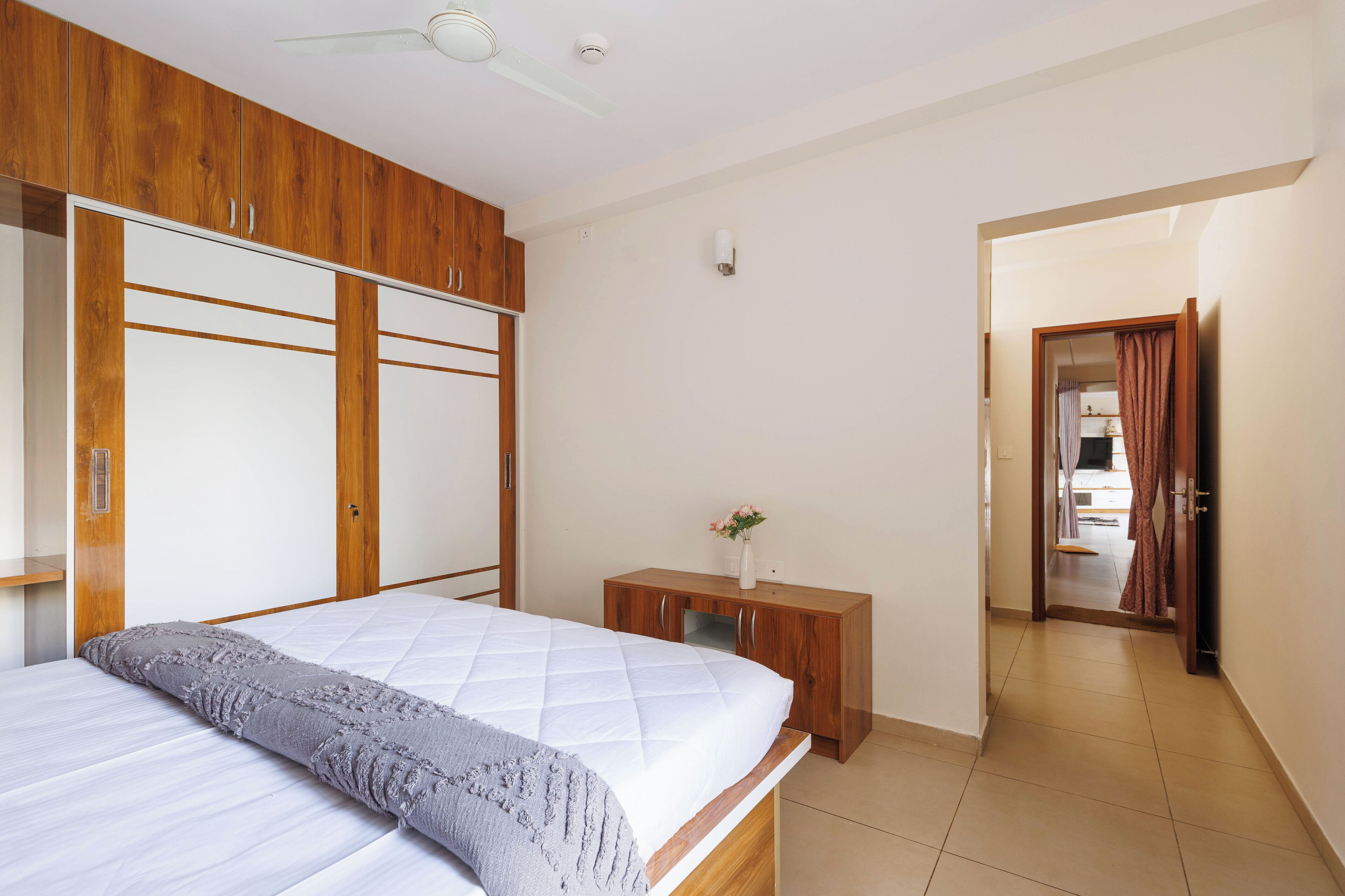 Une chambre à coucher comprenant un lit, une armoire en bois, une table de chevet et une porte donnant sur une autre pièce.