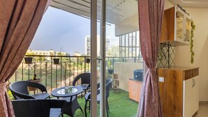 A balcony with a dining table and chairs, a small kitchen area, and a view of buildings in the distance. - Willow Height by Red Olive30min to Airport Veg (Bengaluru)