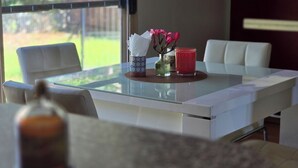 Ein Essbereich mit einem Tisch aus Glas, weißen Stühlen und einer Vase mit rosa Blumen.