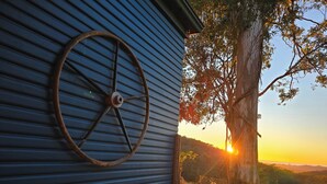 Ein rustikales Rad an einer blauen Metallwand, im Hintergrund Bäume und ein Sonnenuntergang.