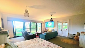 Ein geräumiges Zimmer mit einem großen Bett, zwei Sofas, einem Fernseher und Blick ins Freie.