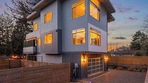 A modern two-story house with a garage, large windows, and a well-lit exterior at dusk. - Bruno House ~ NFL Luxury Home w AC ~ 2 Hot Tubs ~ Game Room ~ Fam Friendly (Seattle)