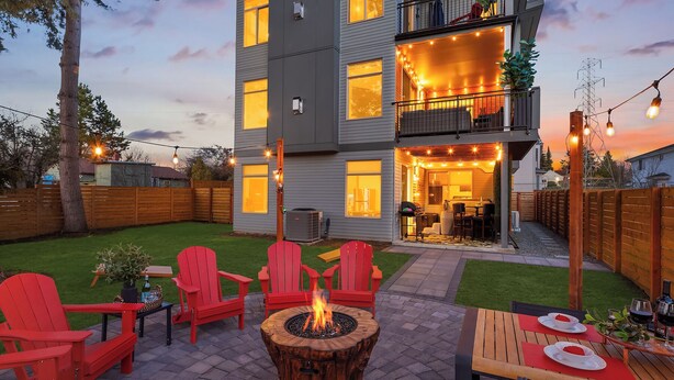 A modern two-story house with a patio area featuring red Adirondack chairs, a fire pit, and a dining table set for two. - Bruno House ~ NFL Luxury Home w AC ~ 2 Hot Tubs ~ Game Room ~ Fam Friendly (Seattle)