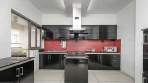 A modern kitchen with black cabinets, a central island, a microwave, and a red backsplash. - Lakeside Aerobay by Red Olive Nr Airport 3bhk (Bengaluru)