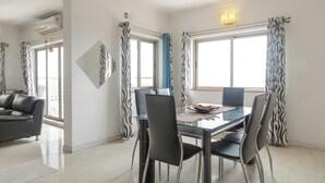 A modern dining area with a glass table, black chairs, and patterned curtains. - Lakeside Aerobay by Red Olive Nr Airport 3bhk (Bengaluru)